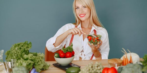 Blonde woman enjoying a fresh salad surrounded by vegetables, promoting healthy eating.