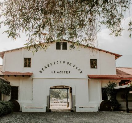 Charming historic building of Beneficio de Cafe La Azotea surrounded by lush greenery and cobblestones.